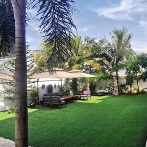 une cour avec une pelouse, des chaises et un parasol dans l'établissement G R A N D C H A L E T, à Salalah