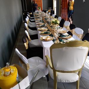 een lange tafel met witte tafels en stoelen bij Suits Guest house & bar in Carletonville