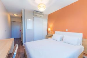 ein Schlafzimmer mit einem weißen Bett und einer orangefarbenen Wand in der Unterkunft Appart’City Confort Montpellier Ovalie I in Montpellier