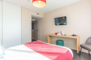 a bedroom with a bed and a desk with a tv on the wall at Appart’City Confort Montpellier Millénaire in Montpellier