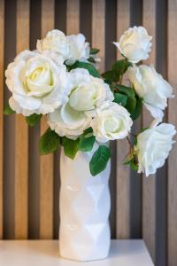 a white vase with a bouquet of white roses at Apartment Leśne Tarasy Dziwnówek by Renters in Dziwnówek