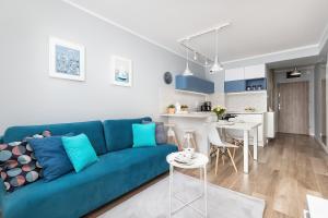 a living room with a blue couch and a kitchen at Apartment Leśne Tarasy Dziwnówek by Noclegi Renters in Dziwnówek +12 photos