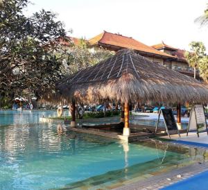 une cabane en paille dans l'eau à côté d'une piscine dans l'établissement Peninsula Beach Resort, à Nusa Dua