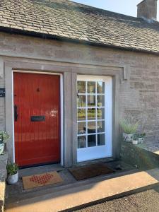 una puerta roja al lado de una casa en Woodview Cottage, en Glamis