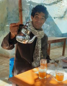 um homem sentado à mesa segurando uma chaleira de chá em Maison d'Hôtes Irocha em Tisseldeï