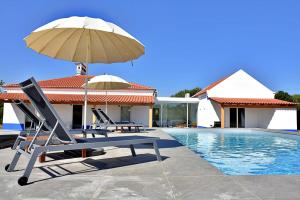 uma piscina com duas espreguiçadeiras e um guarda-sol em Monte Casa Branca em Montemor-o-Novo