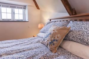 a bed with blue and white sheets and a window at UpAlong Cottage - HiddenDevon in Winkleigh