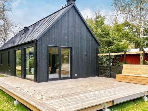 ein schwarzes Haus mit einer Holzterrasse im Hof in der Unterkunft Holiday home HJÄRNARP III in Hjärnarp