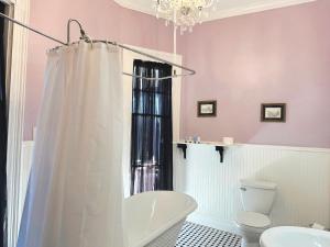 a bathroom with a tub and a toilet and a chandelier at The Mansion on 17th, formerly Schaefer Haus in Galveston