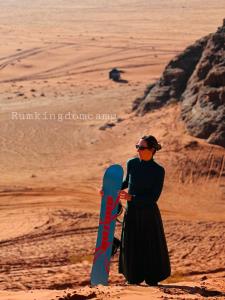 una mujer parada en el desierto sosteniendo una tabla de snowboard en Rum Kingdom Camp en Wadi Rum
