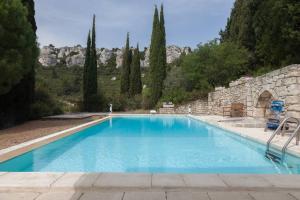 a large blue swimming pool with a stone wall and trees at Mas de Baubesse: Paradise in Provence in Les Baux-de-Provence