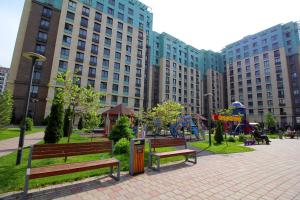 un parc avec des bancs, une aire de jeux et des bâtiments dans l'établissement 2-комнатная квартира в ЖК Гагарин Парк, à Almaty