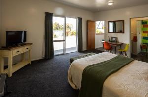 a hotel room with a bed and a television and a desk at GLENALMOND Historic Homestead & Alpine Country Stay in Harihari