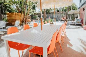 una mesa blanca con sillas naranjas y sombrilla en Pink Paradise Inn - 5 BR Fun Retro Home w/ Pool, en Oceanside