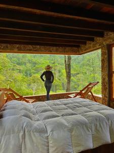 a woman in a hat standing in a bedroom with a large window at Atarisi Lodge in Rurrenabaque
