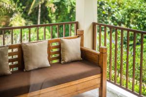 un banco de madera con 2 almohadas en el porche en Swahita Ubud en Ubud