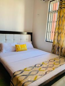 a bed with a yellow pillow and a window at Lux Suites Mahesh Doshi Apartments Nyali in Mombasa +5 photos