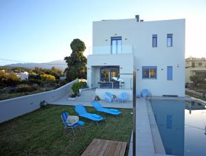 a white house with blue chairs and a swimming pool at Ciel Villa in Kalyves