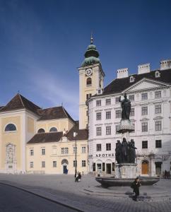 un grand bâtiment avec une tour d'horloge et une statue dans l'établissement Benediktushaus im Schottenstift, à Vienne