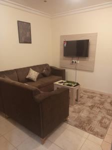 un soggiorno con divano marrone e TV a schermo piatto di VIP For Apartment - شقق فاخره a Al ‘Awālī