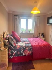 a bedroom with a bed with a red comforter and a window at Halekulani Devon Homestay in Torquay