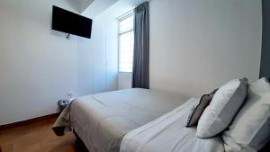 1 dormitorio con 1 cama con sábanas blancas y ventana en Majhu Hostal, en Tacna