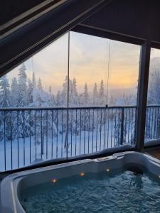 a hot tub on a balcony with snow covered trees at Huvila Hukanhuippu in Syöte