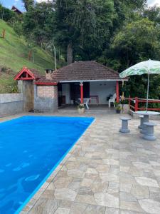 a house with a blue swimming pool and an umbrella at Pousada Cantinho da Paz in Itatiaia