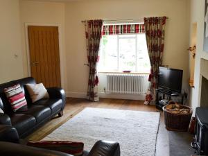 a living room with a leather couch and a television at Clematis Cottage in Burnsall