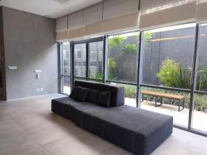 sala de estar amplia con sofá negro y ventanas grandes. en Lindo studio em Moema, en São Paulo