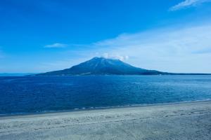a mountain in the middle of the water with a beach at Guest House CARAPAN in Kagoshima