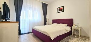 Schlafzimmer mit einem Bett mit einem lila Kopfteil und einem Fenster in der Unterkunft Apartament momA Oradea in Oradea