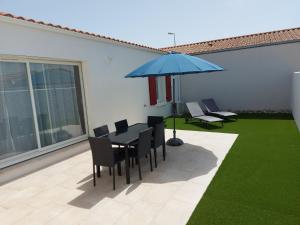 eine Terrasse mit einem Tisch, Stühlen und einem Sonnenschirm in der Unterkunft A bâbord : maison chaleureuse à 300m de la plage in La Cotinière