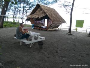 a man sitting on a picnic table next to a hut at Tammoyo Place in Kudat