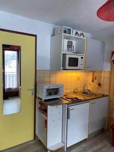 eine Küche mit weißen Schränken, einer Spüle und einer Mikrowelle in der Unterkunft Charmant appartement au pied des pistes de Lelex in Lélex