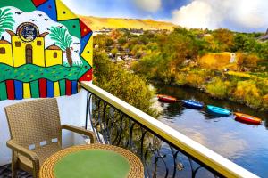 einen Balkon mit einem Stuhl, einem Regenschirm und einem Fluss in der Unterkunft Onaty Ka Guest House in Assuan
