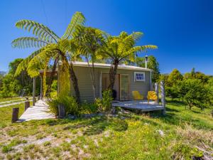 a small house with two chairs and a palm tree at Bay Cottage - Takaka Holiday Unit in Takaka