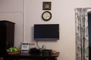 a tv on a wall with a clock and a table at Reunion Pride Villa in Udupi