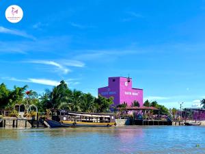 una barca sull'acqua di fronte a un edificio rosa di Rooster Mekong Garden & Villas a Ben Tre