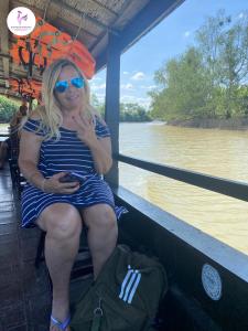 Una donna seduta su una barca su un fiume di Rooster Mekong Garden & Villas a Ben Tre