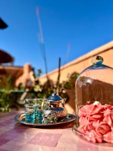 una mesa con un frasco de cristal y un plato de flores rosas en Riad Lauriers Blancs, en Marrakech