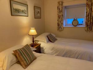 two beds in a bedroom with a window and a lamp at Little Reeds in Bovey Tracey
