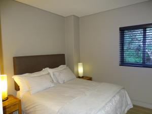1 dormitorio con 1 cama con sábanas blancas y ventana en Chapman's Peak Penthouse en Hout Bay
