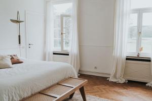 a white bedroom with a bed and two windows at Bleyckhof in een uniek natuurgebied in Ranst