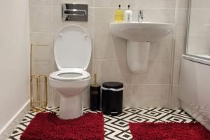a bathroom with a toilet and a sink and red rugs at Luxury New Flat, 5mins from Lakeside Mall in West Thurrock