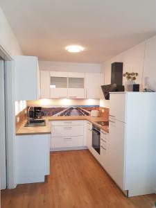 a white kitchen with white appliances and wooden floors at Ferienwohnung MeerBlick OG in Altefähr
