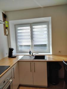 a kitchen with a sink and a window with blinds at Charmante petite maison proche du bourg in Le Bourgneuf-la-Forêt