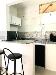 una cocina con armarios blancos y taburetes negros en Flat por temporada, en São José da Coroa Grande