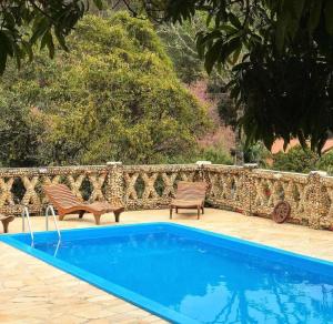 a swimming pool with two chairs and a stone wall at Pousada Meu Recanto in Conceição da Ibitipoca