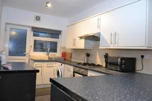 cocina con armarios blancos y encimera negra en Cozy home near city, sleeps 5, Free Parking, WIFI, en Liverpool